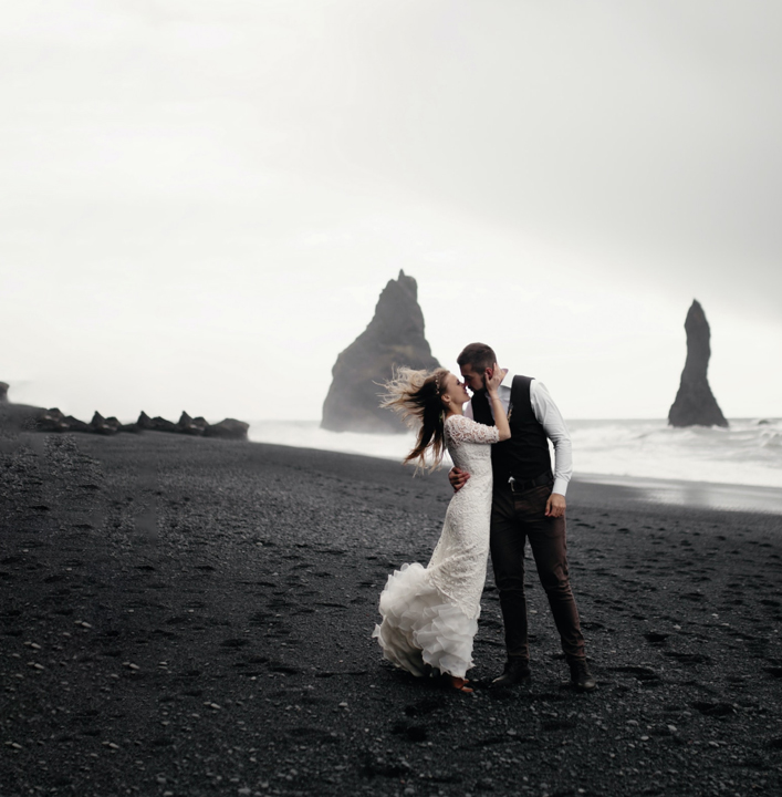 Bride and groom kiss on windswept beach
