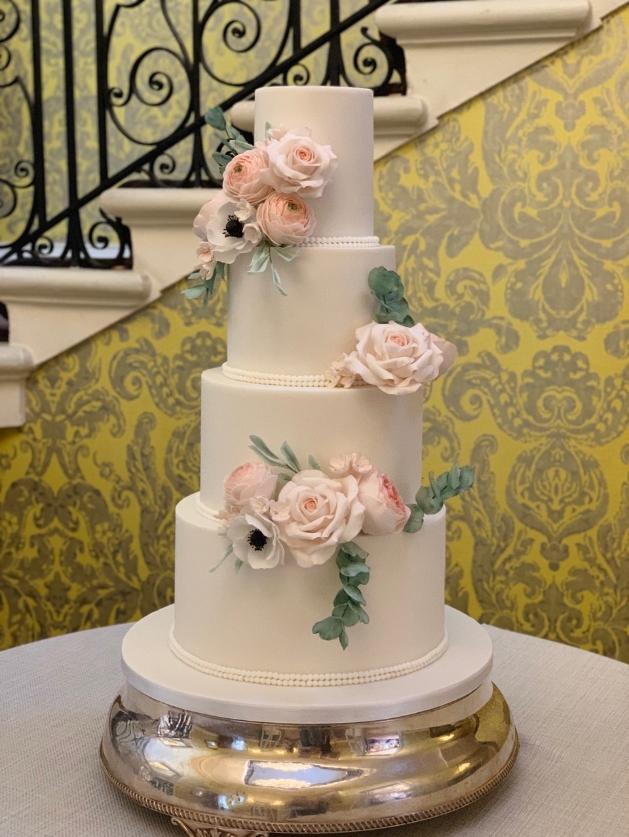 Four tier wedding cake decorated with roses pictured in front of a grand staircase