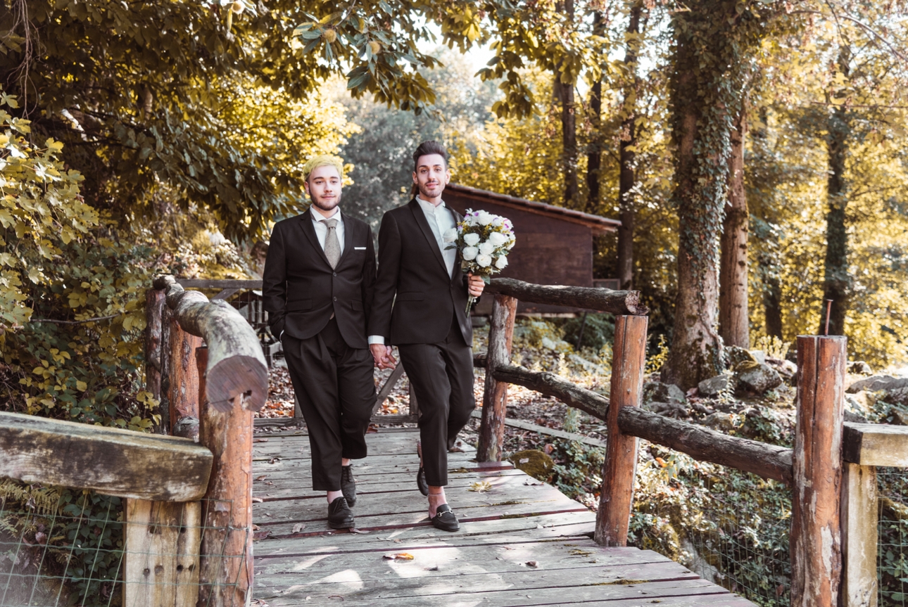 Grooms walk across wooden bridge in woods