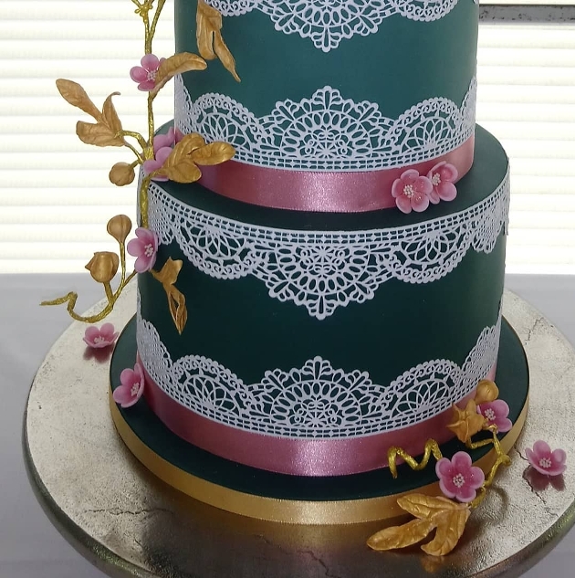 teal coloured layered cake with white lace pattern overlay decorated with flowers