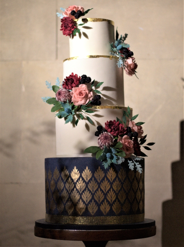 four tiered layer cake design, bottom tier navy and gold, three white tiers, adorned with flowers