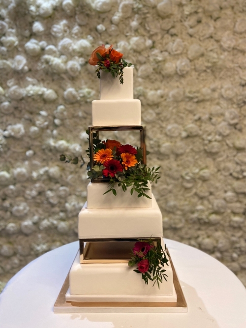 four tiered square layer cake with two fake tier of perspex glass, flowers on top