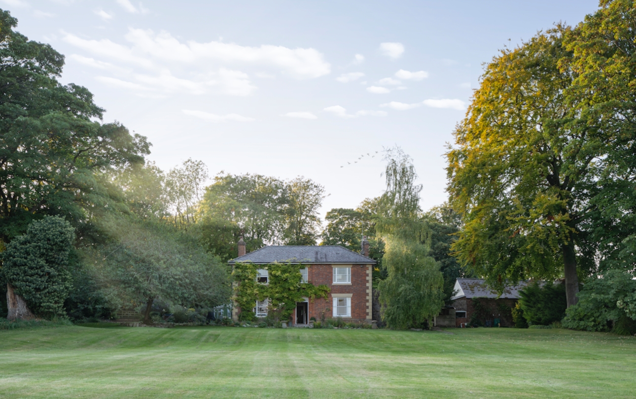 red brick country house surrounded by woodlands and large lawn