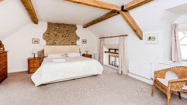 large bed in a white walled beamed ceiling room with chair and chest of drawers