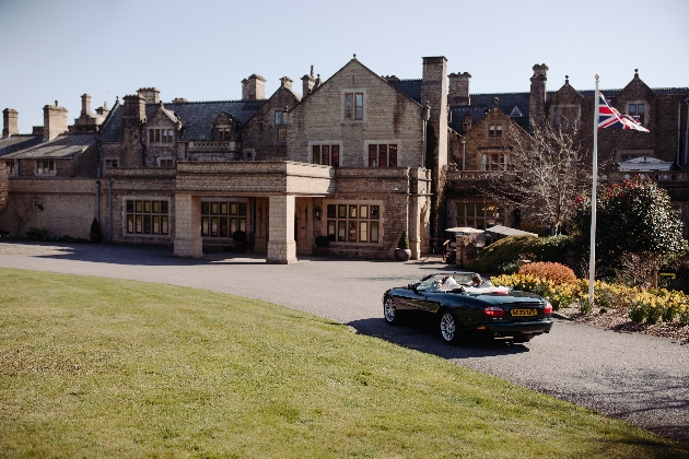 historic house with soft top car driving up to it with bride and groom in
