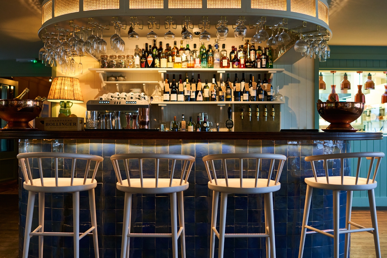 circular central bar, with blue tiles, four bar stools, glasses hanging above