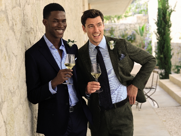 Two men wearing suits while laughing and holding glasses of wine