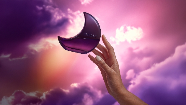 lifestyle shot of ghost fragrance and hand reaching towards it against a background of purple clouds