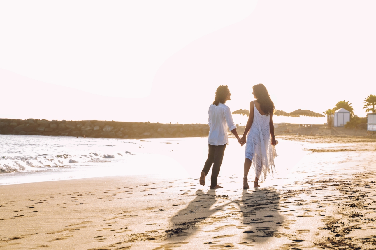man and woman walking on the beach at sunset