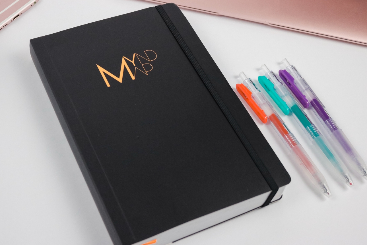 black journal laying next to three coloured gel pens