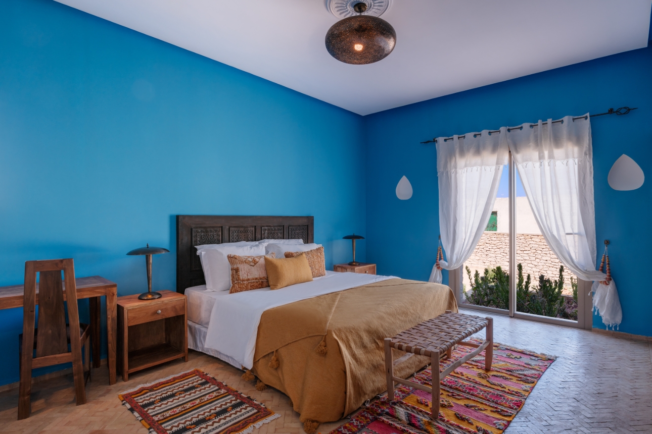 Blue bedroom with central large bed, rugs on floors
